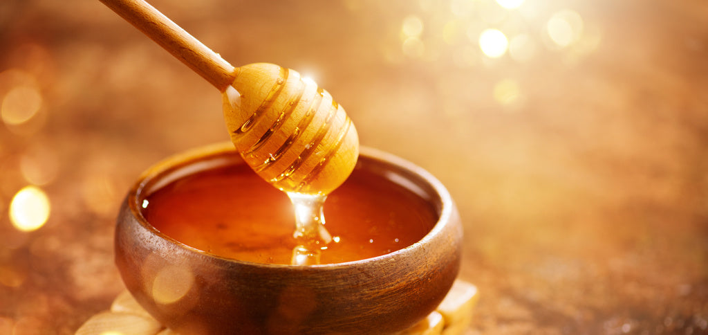 A honey dipper being dipped into a bowl of honey
